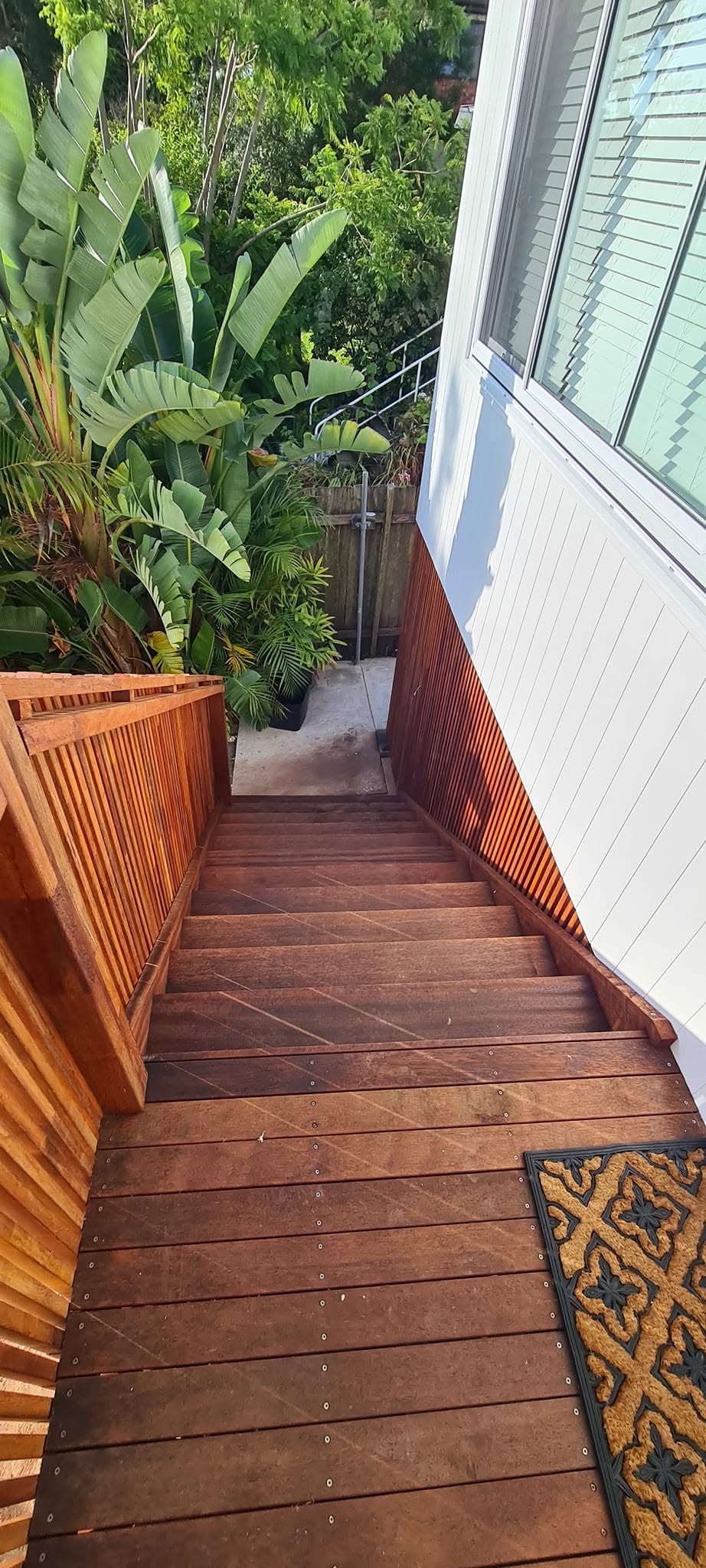 Timber stairs and vertical slat balustrade beside a renovated home